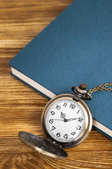 Vintage pocket watch clock with book on wooden background