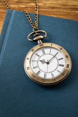 Vintage pocket watch clock with book on wooden background