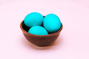 Three Easter eggs of turquoise color in a wooden plate on a soft pink background.