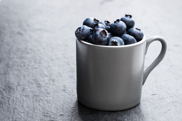 Cup full of fresh ripe blueberries on black stone background