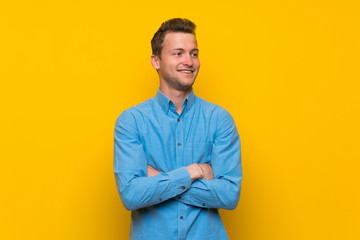 Blonde man over isolated yellow wall happy and smiling