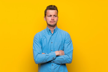 Blonde man over isolated yellow wall with confuse face expression