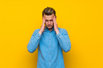 Blonde man over isolated yellow wall with headache