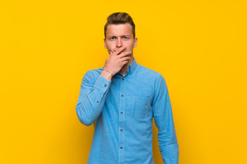 Blonde man over isolated yellow wall surprised and shocked while looking right