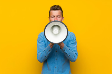 Blonde man over isolated yellow wall shouting through a megaphone