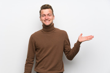 Blonde man over isolated white wall holding copyspace imaginary on the palm to insert an ad