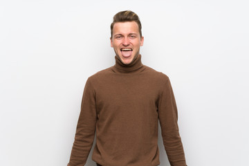 Fototapeta premium Blonde man over isolated white wall showing tongue at the camera having funny look