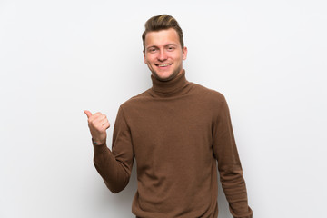 Fototapeta premium Blonde man over isolated white wall pointing to the side to present a product