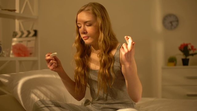 Young woman crossing fingers holding pregnancy test hand, birth control methods