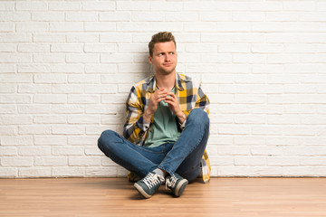 Blonde man sitting on the floor scheming something