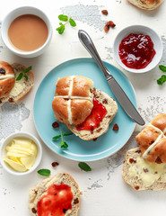 Hot cross buns in blue plate served with butter, strawberry jam and cup of tea