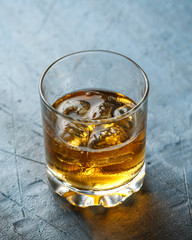 Glass of whiskey with ice on rustic background