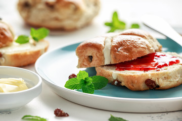 Hot cross buns in blue plate served with butter, strawberry jam and cup of tea