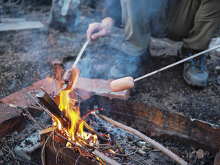 the man is grilling sausages on the fire at night. Fire and flame sausages are fried to a tender crisp
