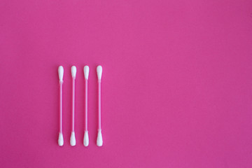 top view on four pink cotton buds with white heads laid out in vertical line on a pink background