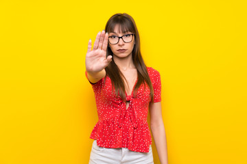Young woman over yellow wall making stop gesture