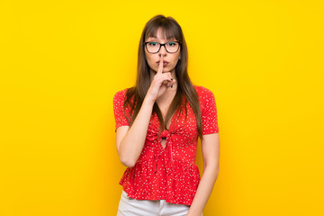Young woman over yellow wall showing a sign of silence gesture putting finger in mouth