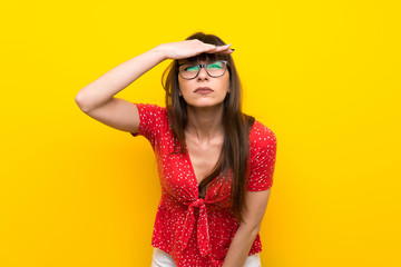 Young woman over yellow wall looking far away with hand to look something