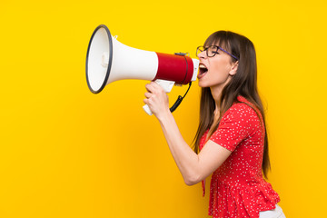 Young woman over yellow wall shouting through a megaphone