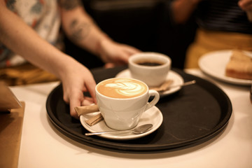 Woman bring two white cups of latte and americano coffe on tray