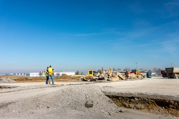 Construction site of road, building or airport with construction machinery (truck, bulldozer, excavator) and construction workers or engineers