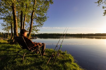 Angler sitting on the shore of the lake during sunrise