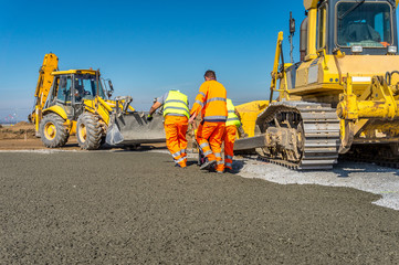 Construction site of road, building or airport with construction machinery (truck, bulldozer, excavator) and construction workers or engineers
