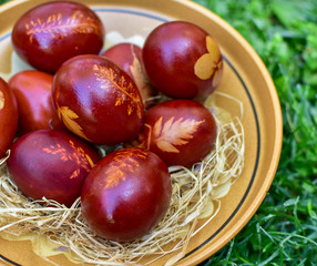 Obraz premium Home made Easter eggs cooked in water with onion peel and natural plant patterns. Eggs are in a clay pot. For the background is green grass.