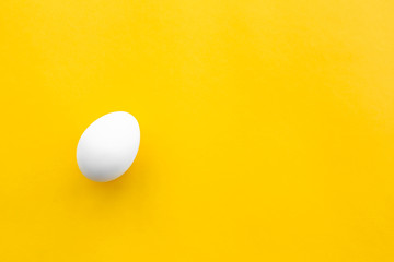 One white chicken egg lies on a yellow background. Healthy organic food and diet concept. Easter...