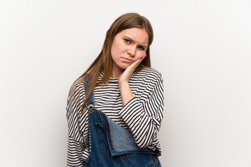 Young woman in dungarees over white wall unhappy and frustrated