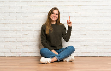 Young woman sitting on the floor showing and lifting a finger in sign of the best