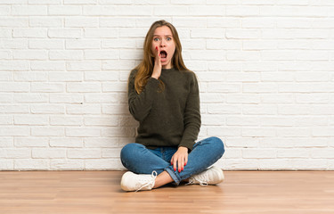 Young woman sitting on the floor with surprise and shocked facial expression