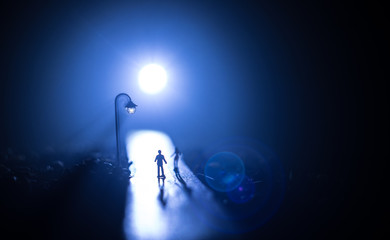 Young couple holding each other hands. Slowly walking under white street lights in night. Dark time. Peaceful atmosphere in mist. Foggy air.