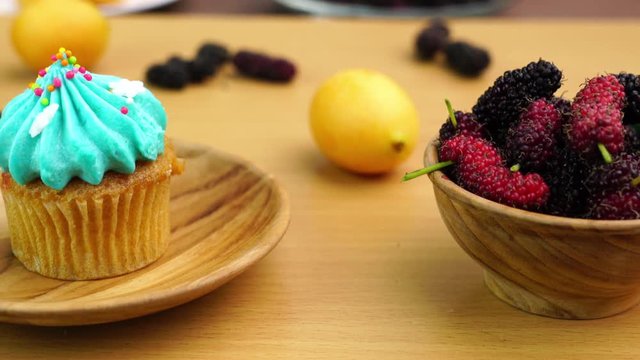 Dilicious Cupcake on a wooden plate with Mulberry and Marian plum in wooden bowl