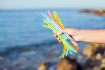 Fototapeta na wymiar Close Up Of Hand Holding Plastic Straws Polluting Beach. Environmental pollution concept