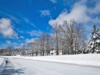 Snow covered street with houses in Minnesota residential community after winter storms with blue sky and a few clouds.