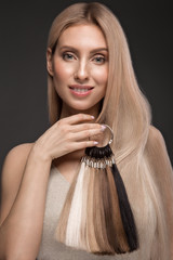 Beautiful blond girl with a perfectly smooth hair, classic make up with a palette for hair extensions in the hands. Beauty face.