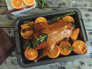 whole roast duck with oranges, stuffed with apples and rosemary on a baking tray