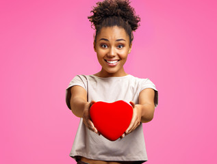 Lovely young girl holds heart shaped gift box. Photo of african american girl wears casual outfit...