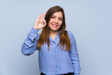 Young girl over isolated blue wall showing ok sign with fingers