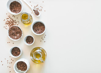 flax seeds and flaxseed oil on white or light beige background. Set of small bowls with organic flax seed or linen seed. Flax oil is rich in omega-3 fatty acid. Copy space. Top view or flat-lay.