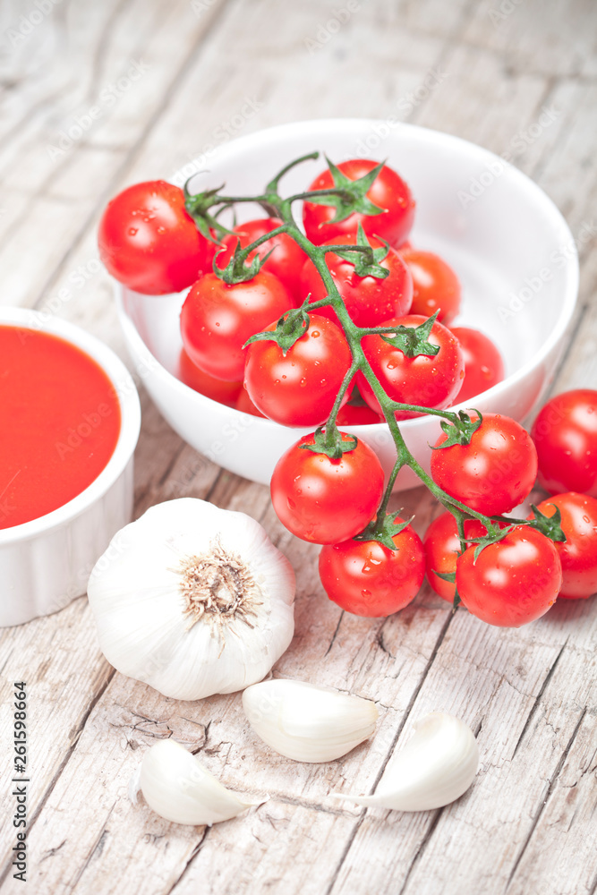 Wall mural fresh tomatoes in white bowl, sauce and raw garlic on rustic wooden table.