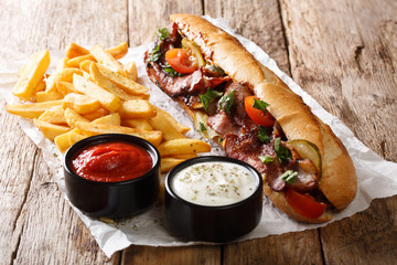 Traditional spicy hot dog with fried bacon, vegetables, french fries and sauces close-up. horizontal