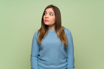 Young girl over green wall making doubts gesture looking side