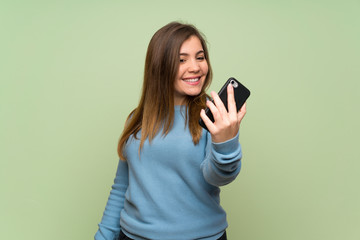 Fototapeta premium Young girl over green wall making a selfie