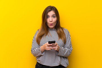 Young girl over yellow wall surprised and sending a message