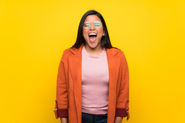Young Colombian girl over yellow wall shouting to the front with mouth wide open