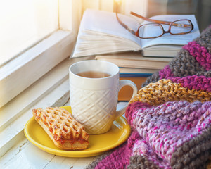 A сup of hot tea, stack of books and glasses on the background of a knitted blanket. 