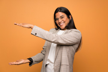 Young Colombian girl over brown wall holding copyspace to insert an ad