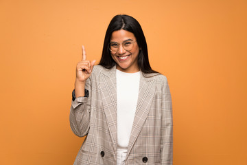 Young Colombian girl over brown wall showing and lifting a finger in sign of the best